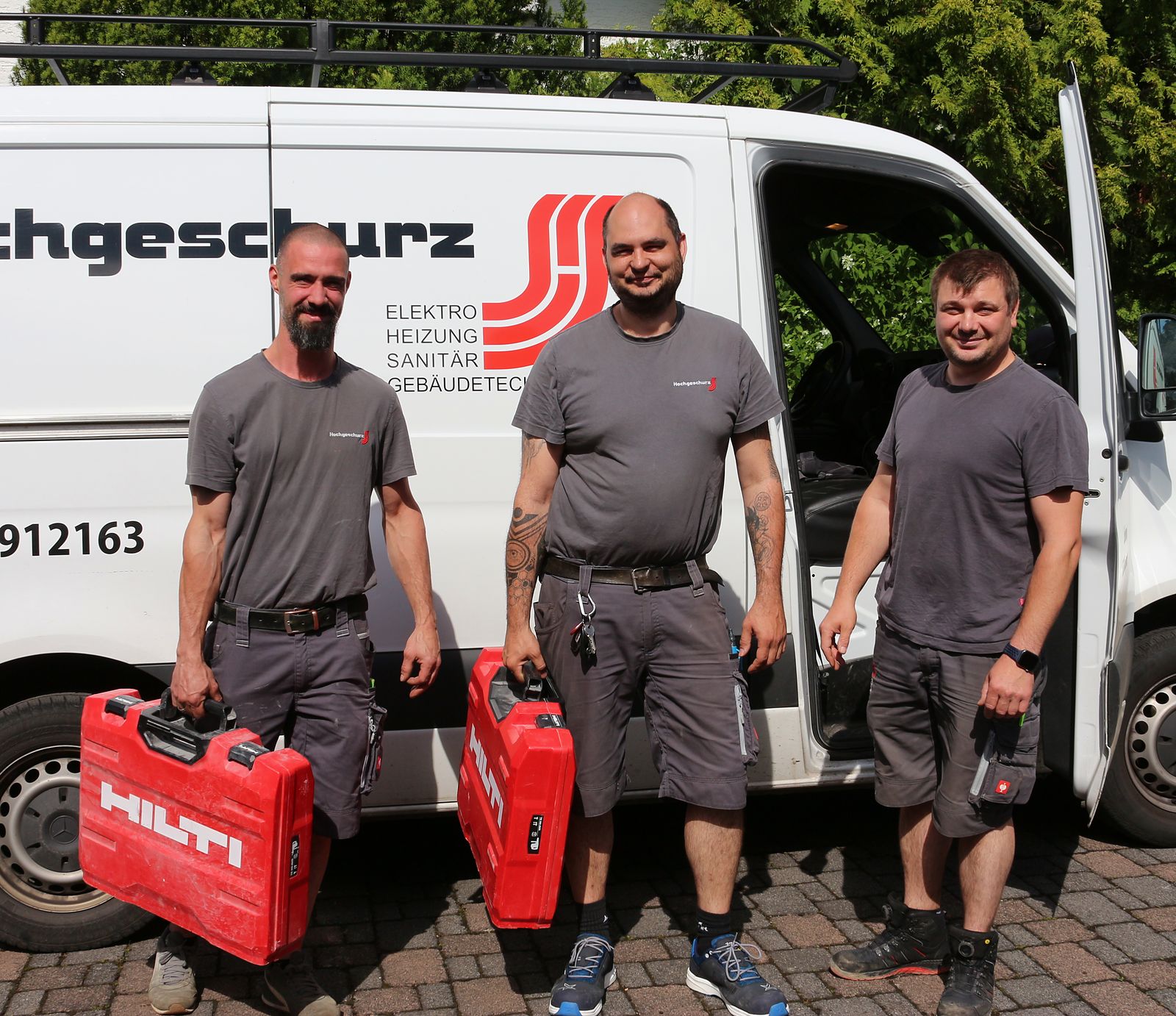 Drei Monteure der Hochgeschurz Haustechnik mit Werkzeugkoffern vor dem Firmenfahrzeug